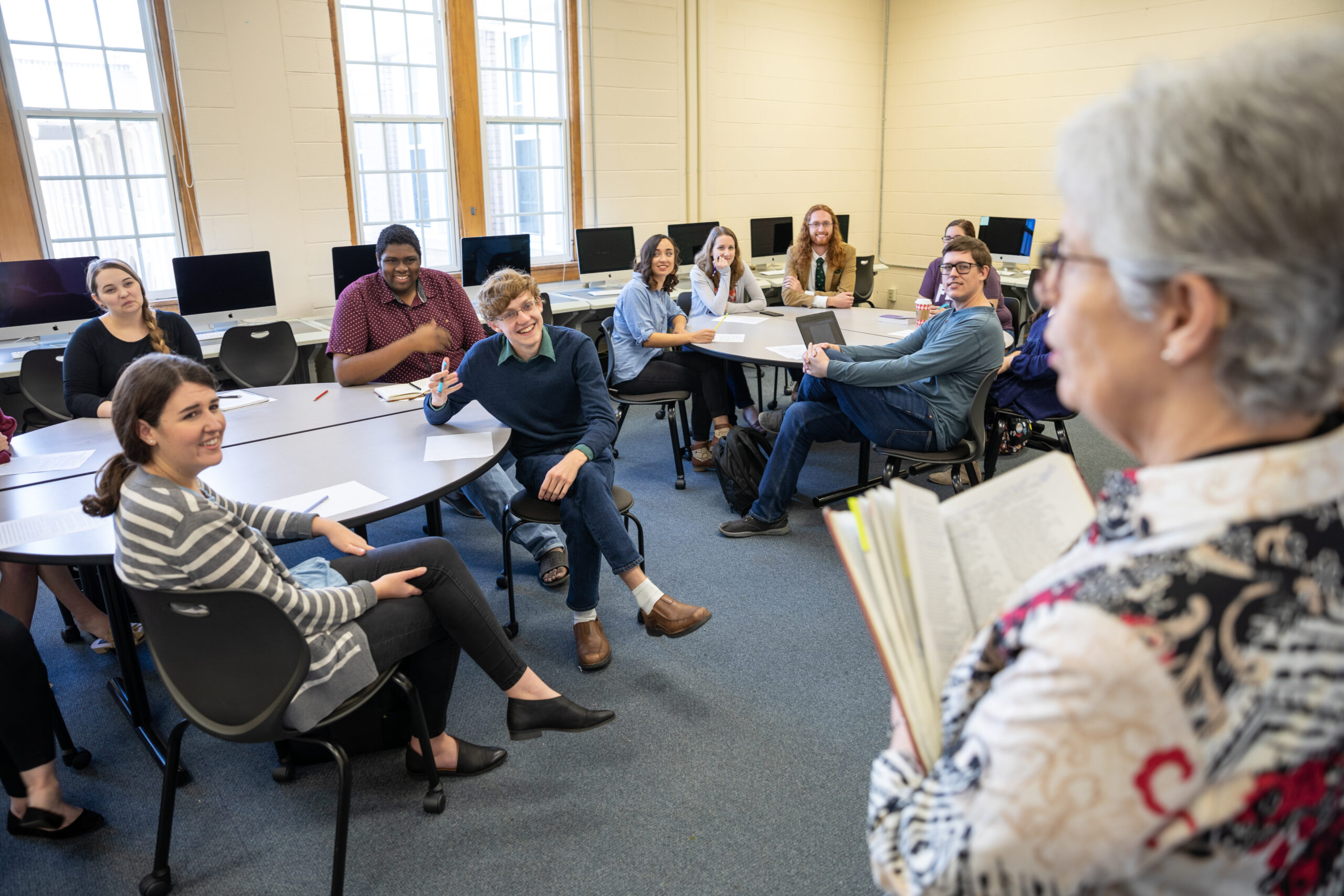 A professor holding an open book facing two groups of literature students
