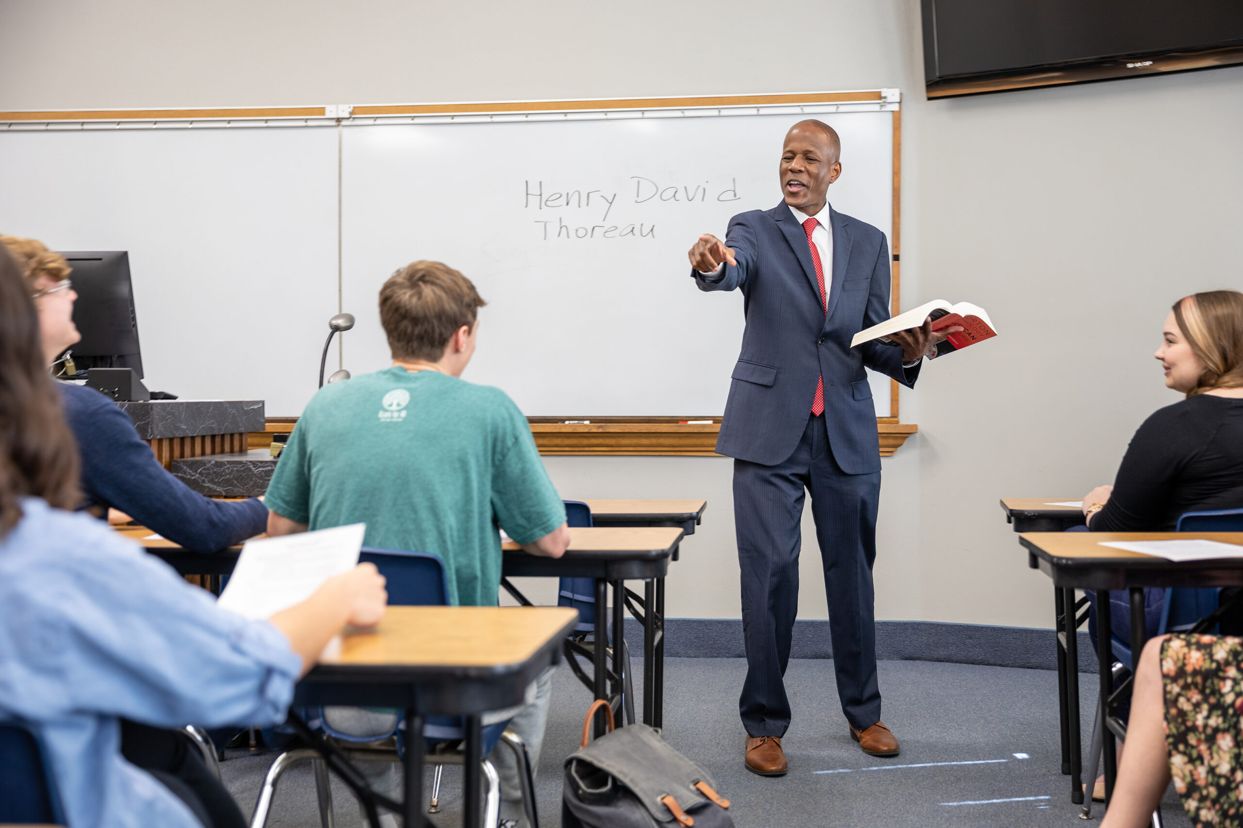 a professor holding an open textbook and talking to the master's students in the classroom