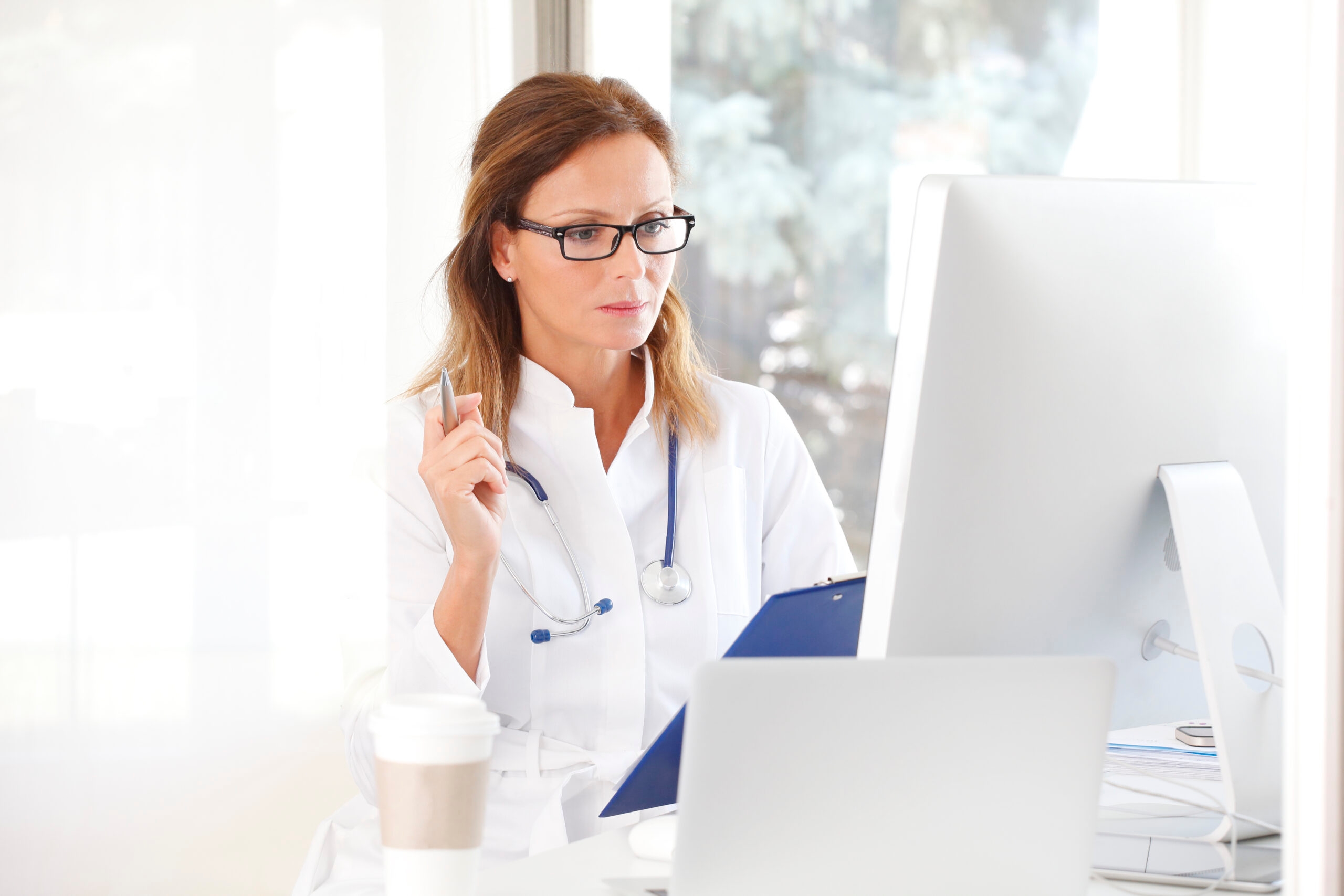 Female doctor writing on clipboard in front of a computer