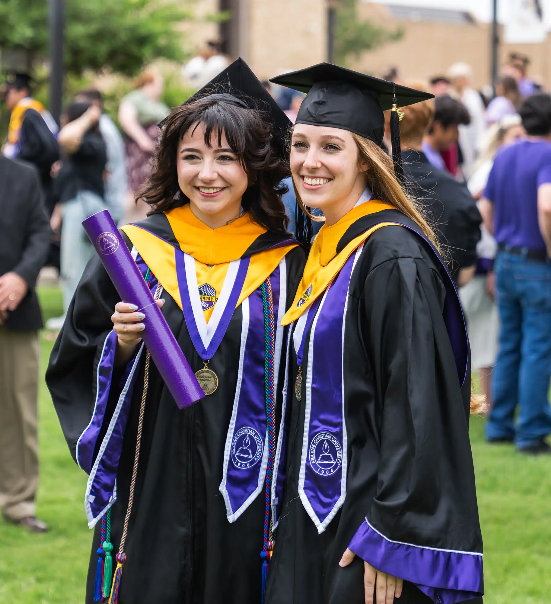 Two students in academic regalia with Honors College distinction pose for a photo after their commencement ceremony.