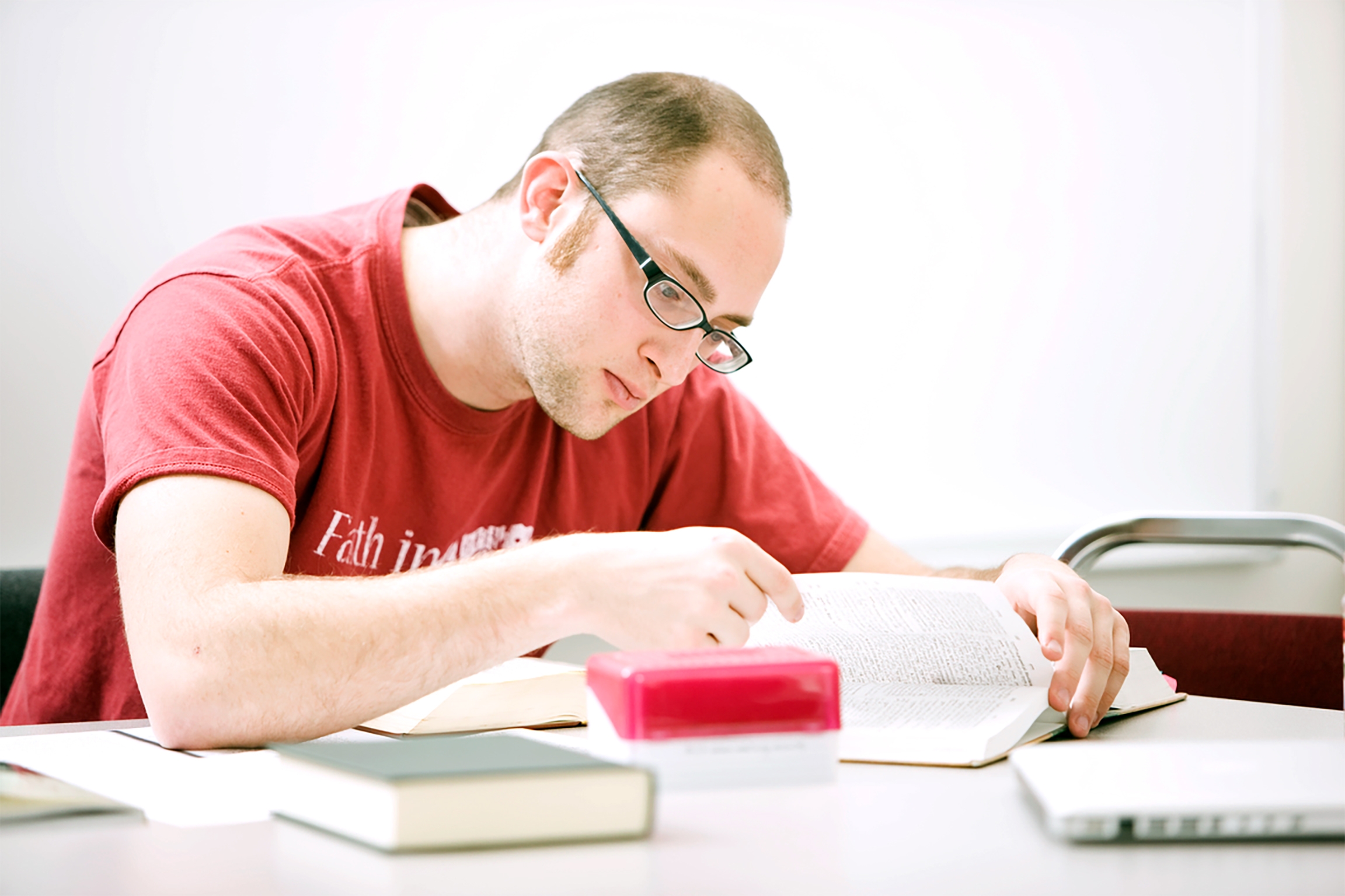 A graduate student in red t-shirt with glasses reading books