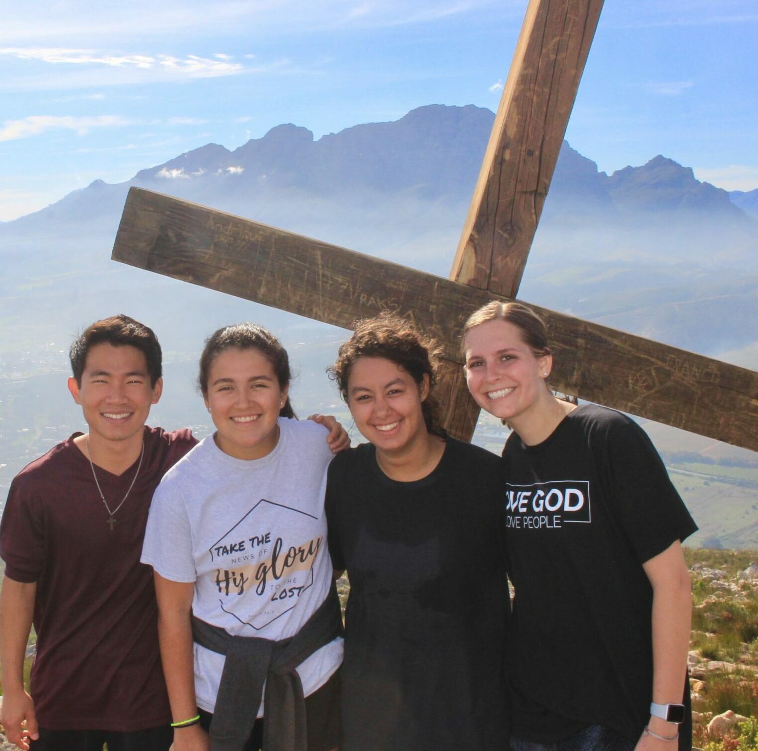 Four ACU students standing in front of a cross