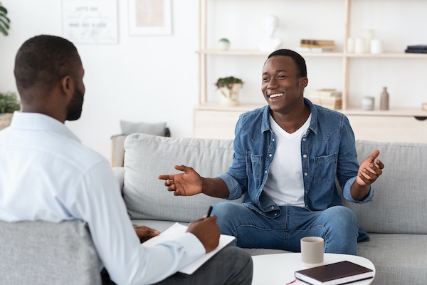 Successful Therapy. Cheerful black man talking to psychologist on meeting at his office, sharing his progress with doctor (Successful Therapy. Cheerful black man talking to psychologist on meeting at his office, sharing his progress with doctor, ASCII
