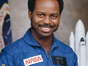 A formal portrait of Dr. Ronald E. McNair in his NASA uniform, with a model space shuttle over his shoulder.