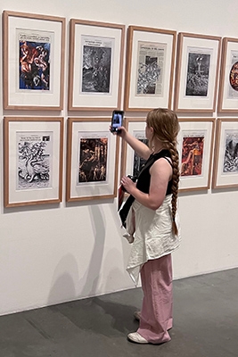 Young woman in an art museum taking a photo on her phone of a piece of art