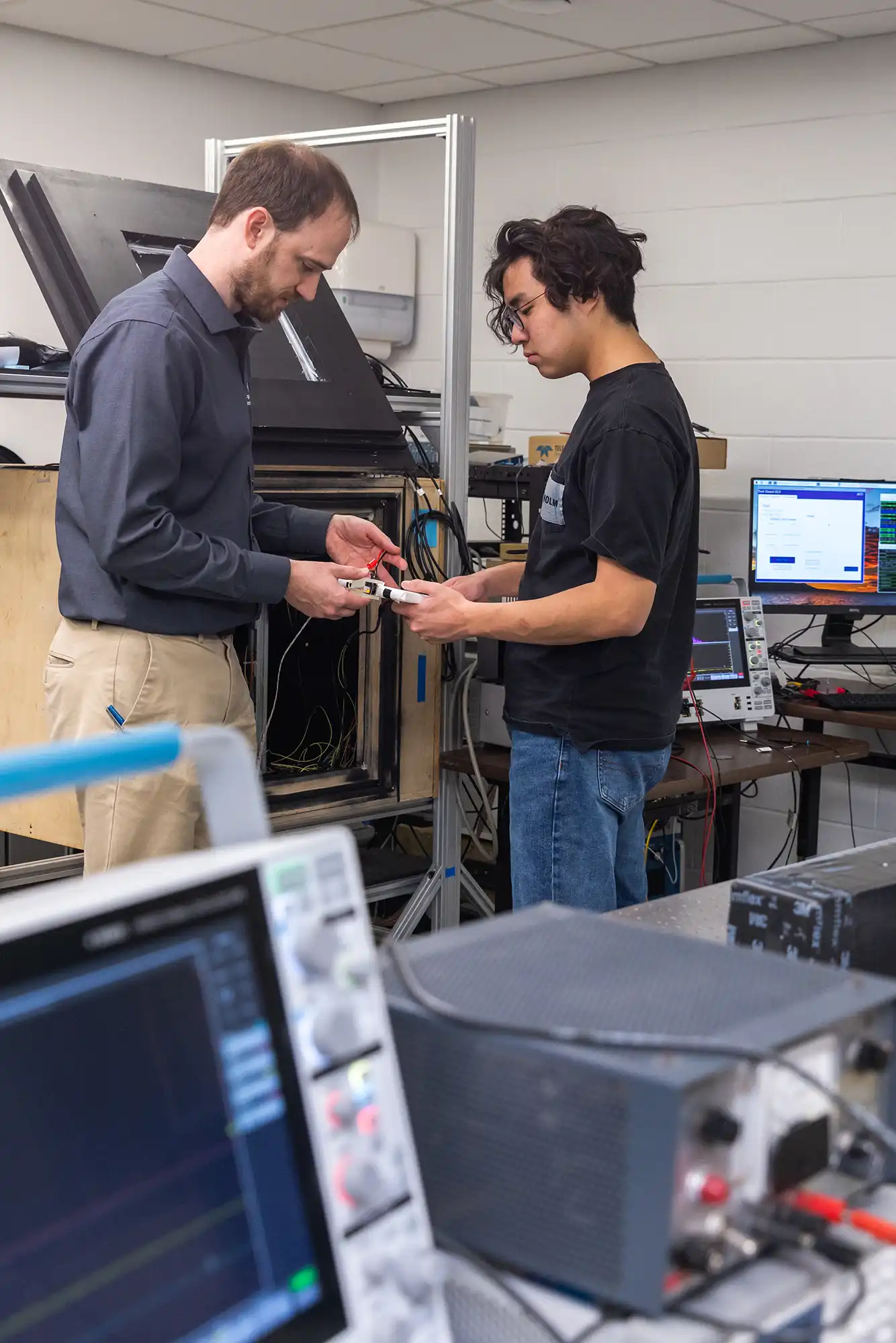 A physics professor and student examine an electronics part together in the lab.