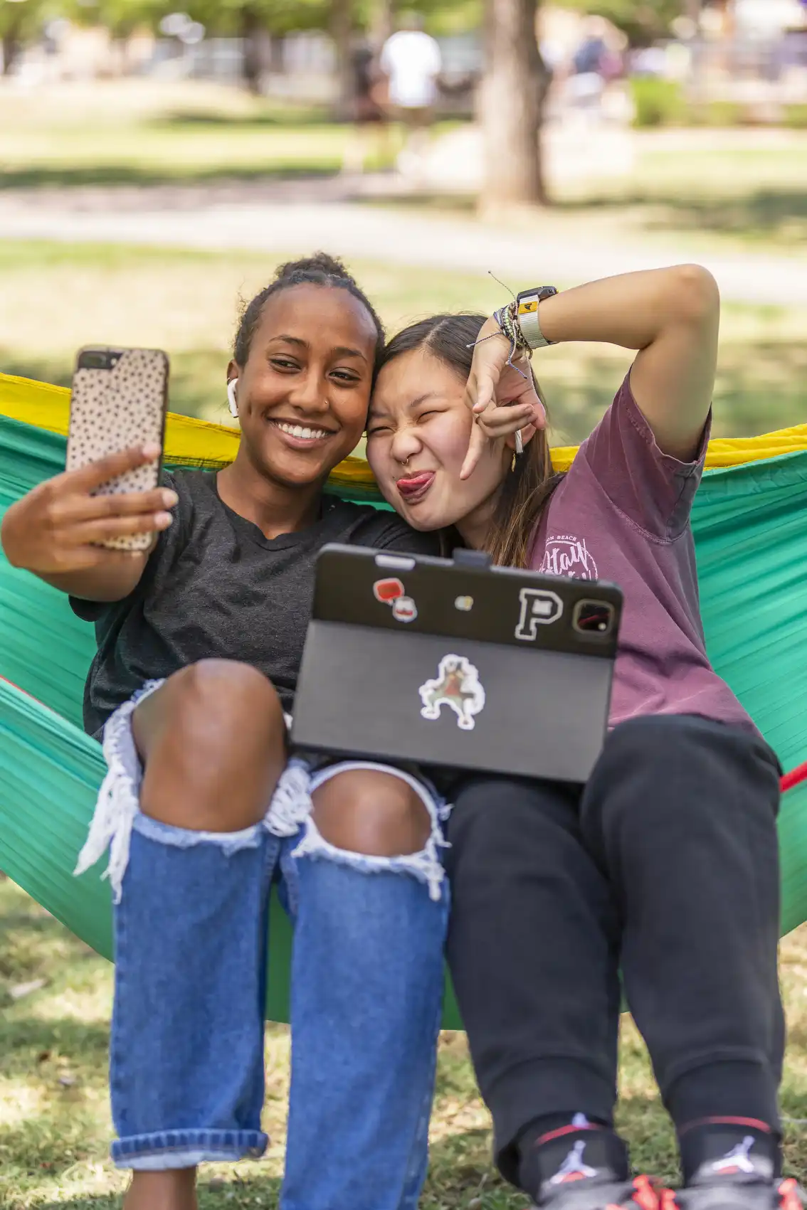 Two students pose for a fun selfie while relaxing in a hammock.