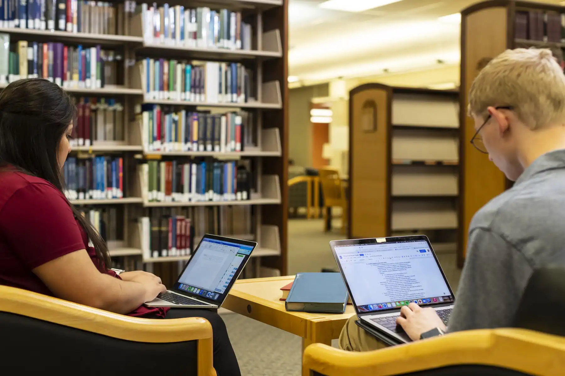 Two students study on laptops inside the library.