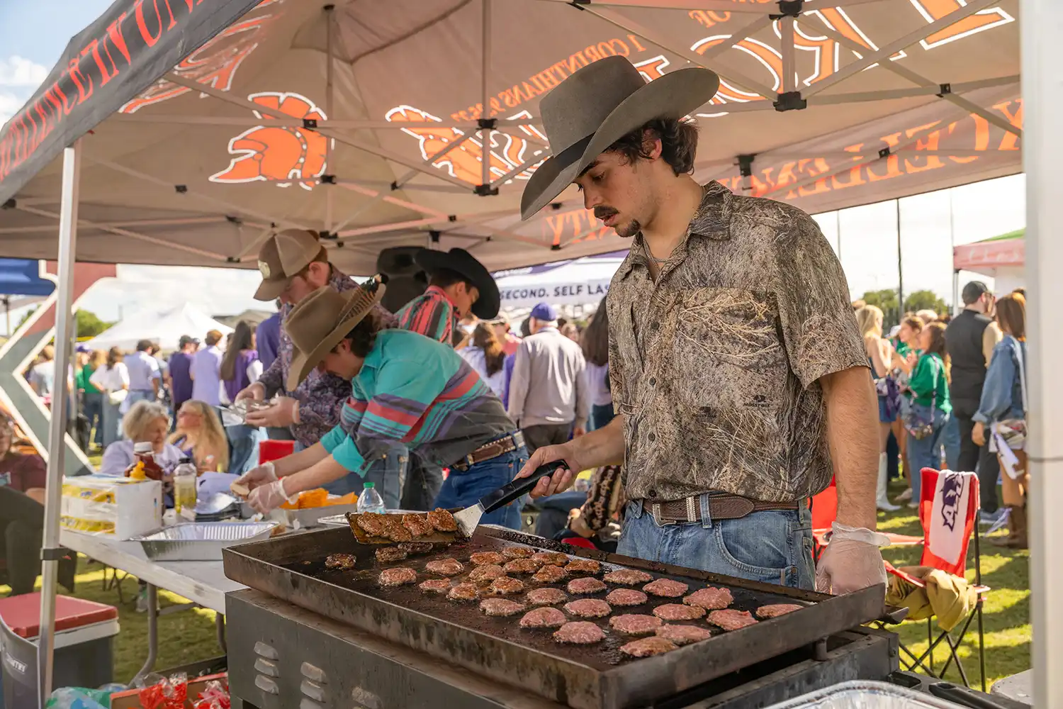 Men of Trojans grilling burgers at a tailgate event.
