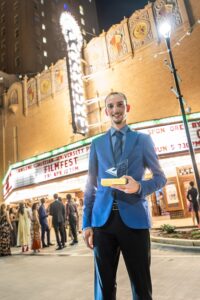Student stands outside Abilene's Paramount Theatre holding an award
