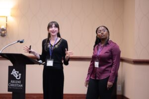 Two students speak in front of a room.