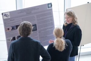 A student stands near an informational poster and talks with two other individuals.