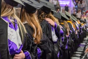 A view from the back of a row of graduates in caps and gowns.