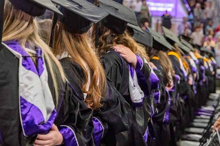 A view from the back of a row of graduates in caps and gowns.
