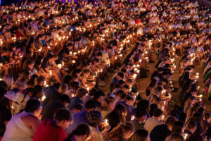 Students sitting in an amphitheatre with heads bowed and lit candles. 
