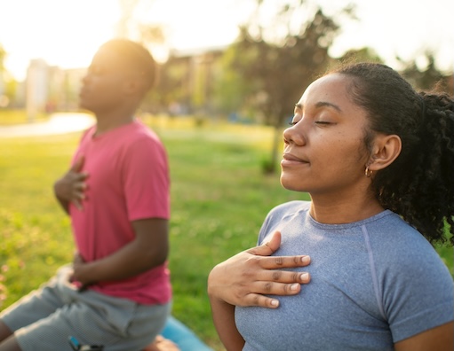Young couple practicing yoga in a summer park, doing breathing exercise