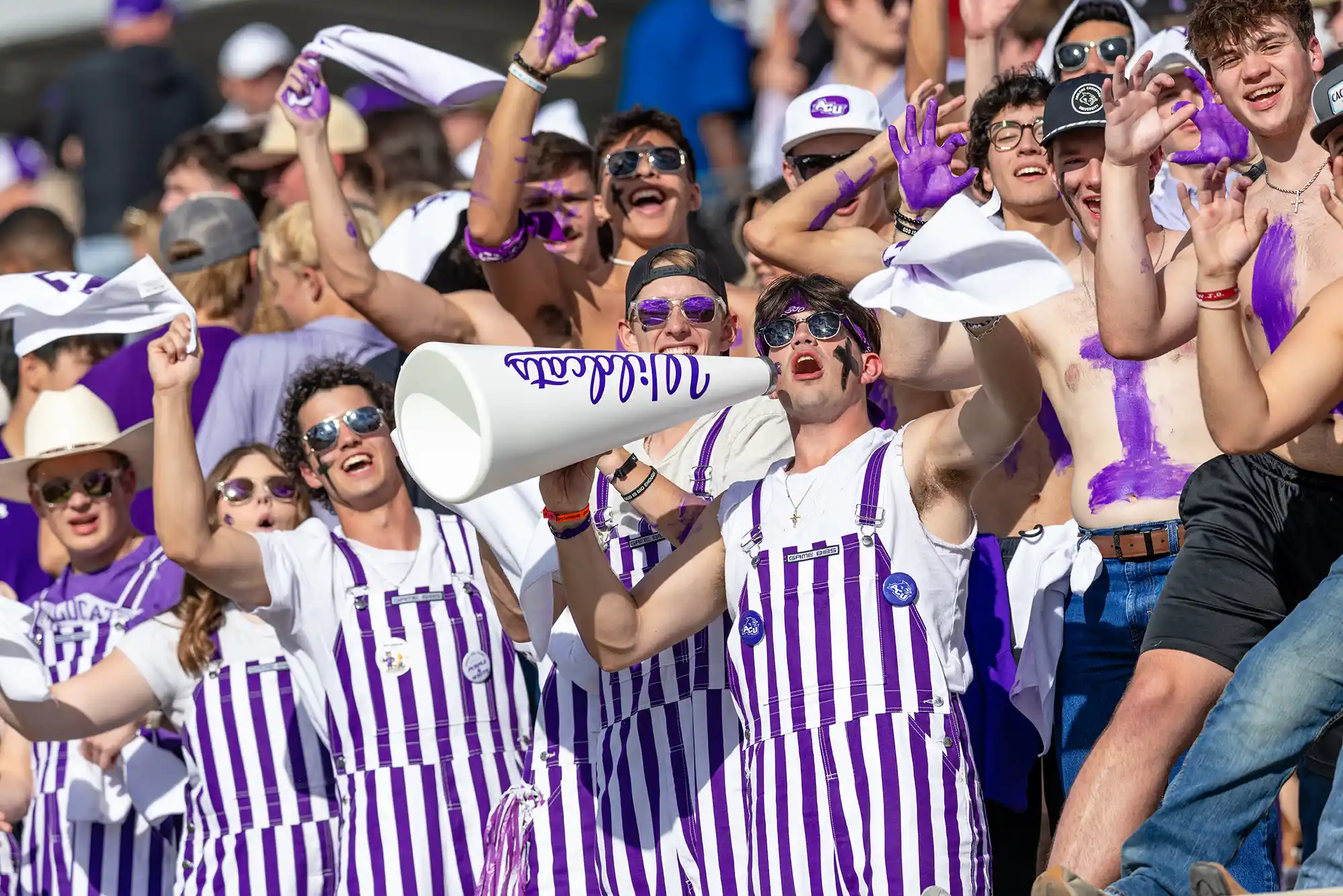 Students dressed and painted in purple cheer on the Wildcats at a football game.