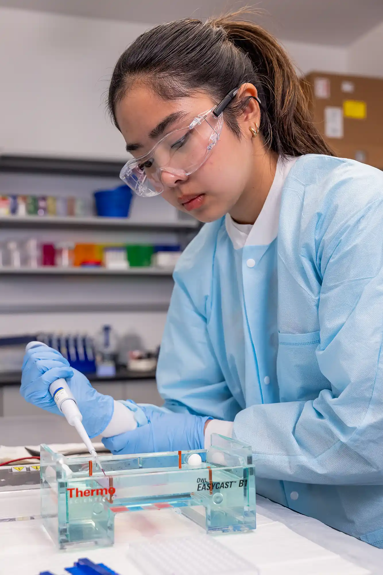 A student dressed in protective lab gear uses a pipette.