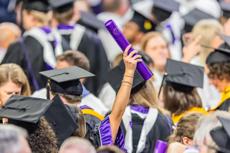 A graduate holds their new diploma high above their head in triumph amidst a sea of graduation caps during Commencement.