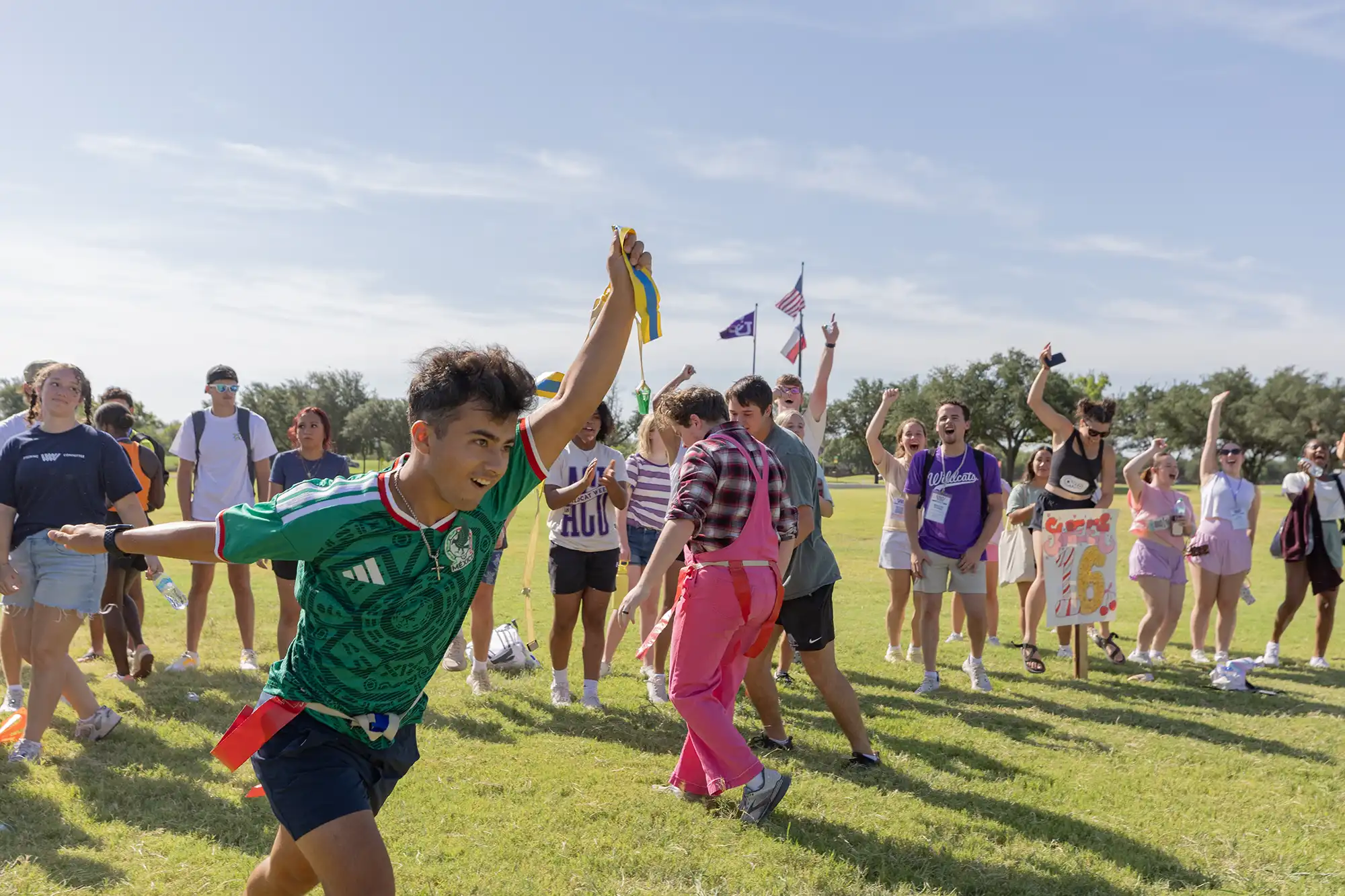 A student holds a flag triumphantly as other students cheer on a race during Wildcat Week.