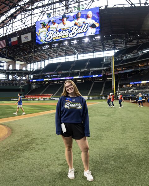 Kaylee Kahn on a baseball field. A screen above says "Banana Ball."